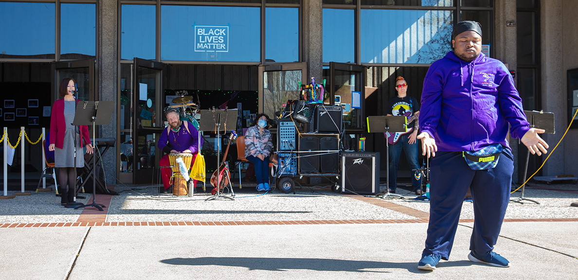 Man wearing purple performs at Coming Alive ceremony while others in background watch