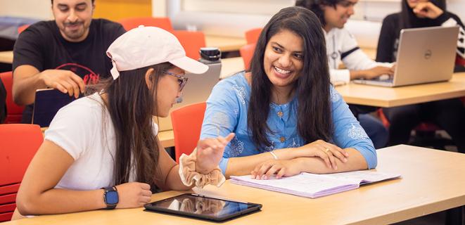 Two females students talk in a classroom