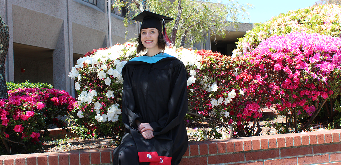 Catherine Thirkill stands in cap and gown on campus
