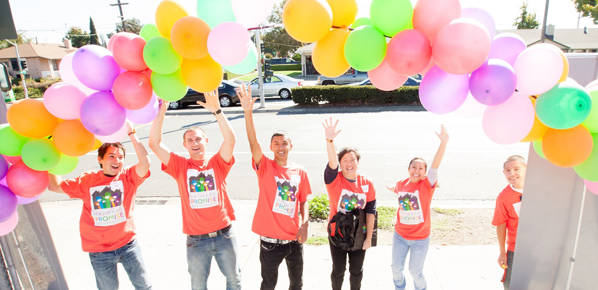 People in red shirts stand with colorful balloon arch