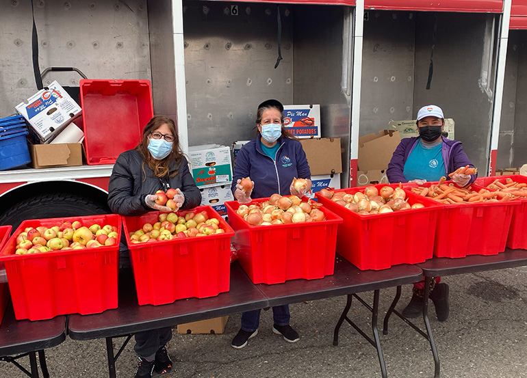 Women with large red food containers full of fresh apples