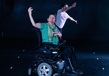 Woman in wheelchair performs on stage with another woman behind