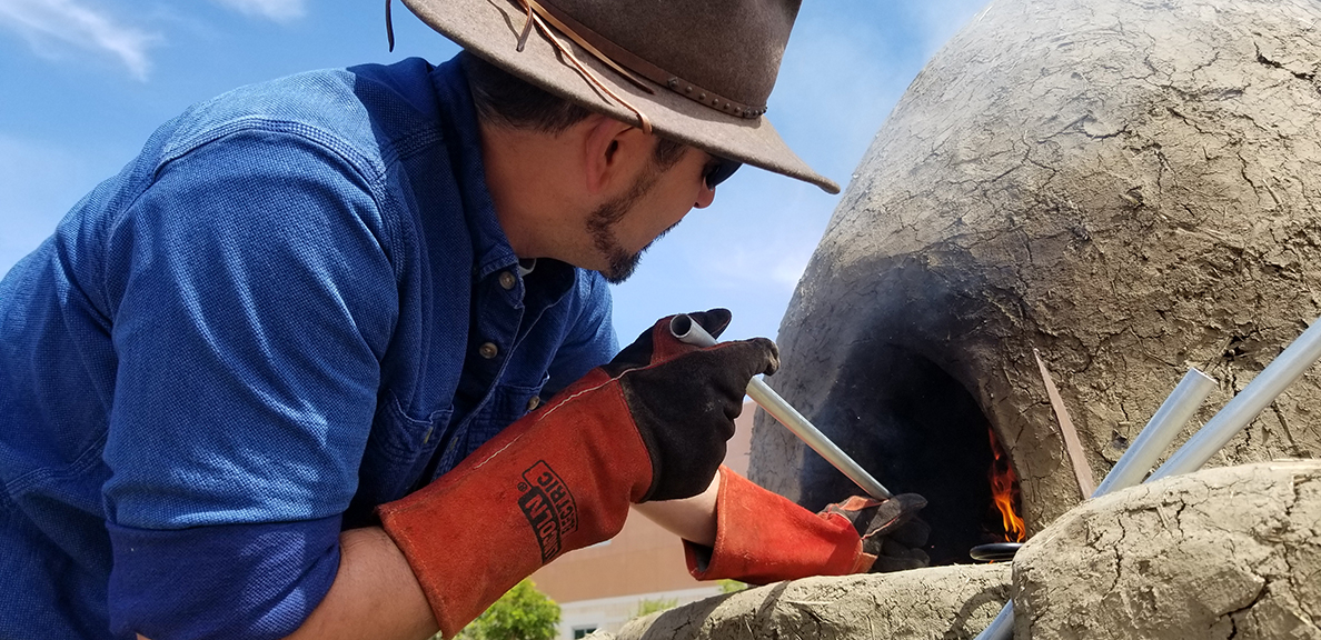 Man in hat puts something in indigenous oven