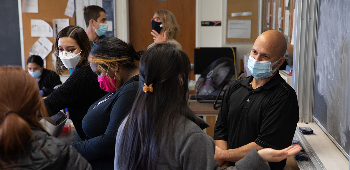 Masked professor and students talk in classroom