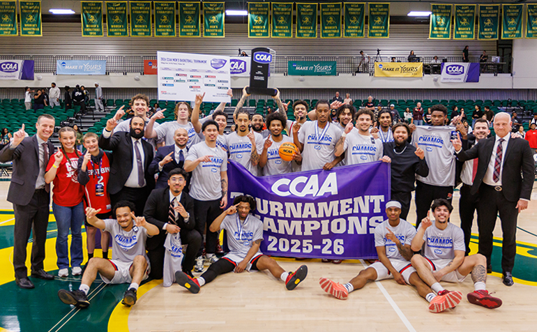A group photo of the Pioneer Men's Basketball team holding a banner reading "CCAA Tournament Champions 2025-26"