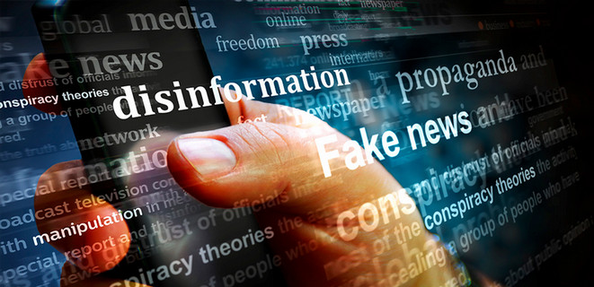 Image of a hand holding a phone with text across the screen, such as "fake news" and "disinformation" 