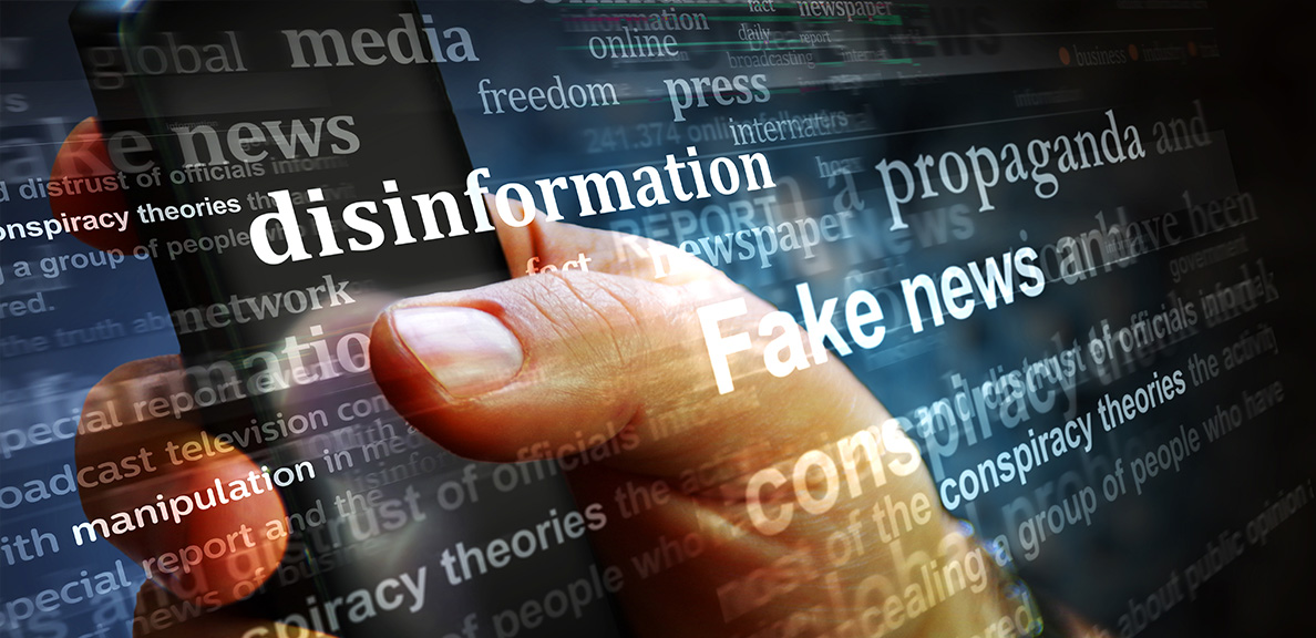 Image of a hand holding a phone with text across the screen, such as "fake news" and "disinformation" 