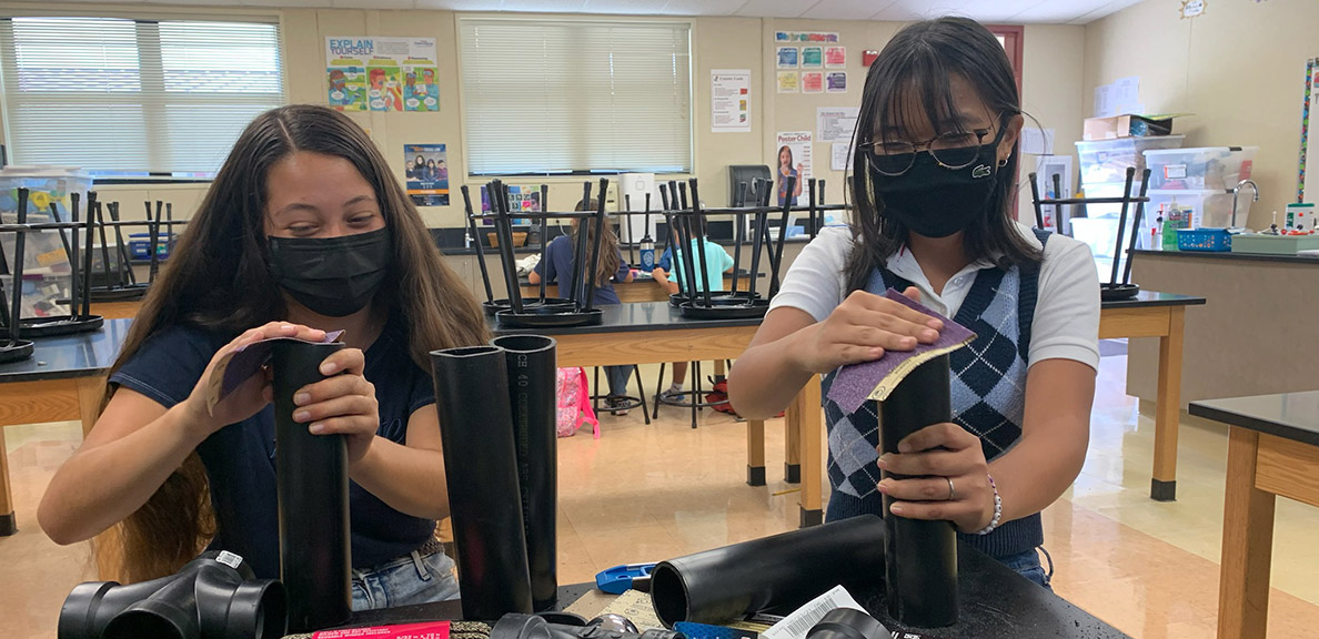 Two students in classroom use PVC pipe on a project