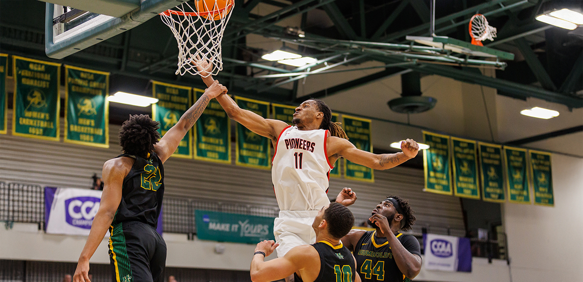 Action shot of Joshua Ijeh shooting the basketball into the net surrounded by three Humboldt defense players. 