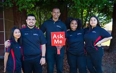 Orientations leaders pose together holding Ask Me sign