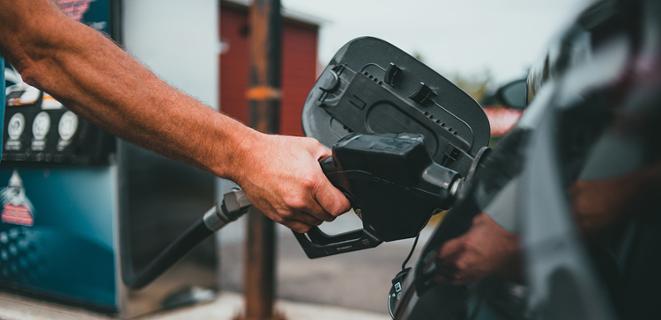 A person's hand putting a gas pump into a car