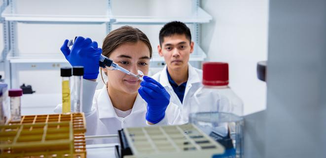 Two student scientists squeezing something into a test tube.
