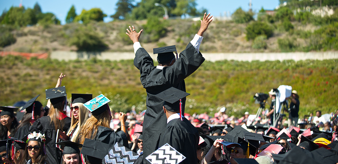 Student raises hands in celebration above other graduates