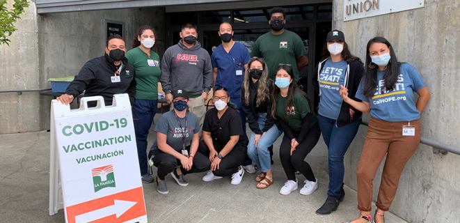 People stand in masks outside a COVID-19 vaccine sign