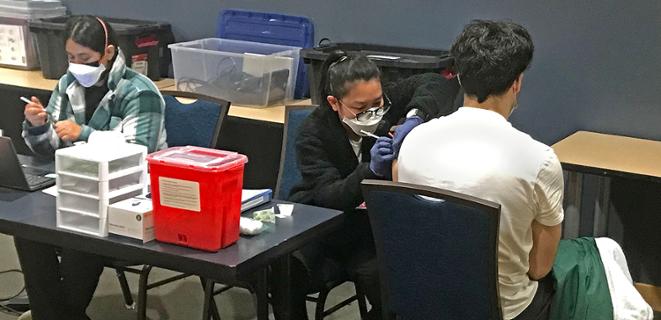 People in masks stand in front of vaccine clinic