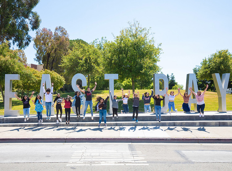 Students jump pose in front of East Bay letters