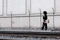 Black and white photo of small woman walking in back of an exaggerated-sized railroad track.