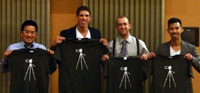 four male students holding black T-shirts, each with a white tripod on it