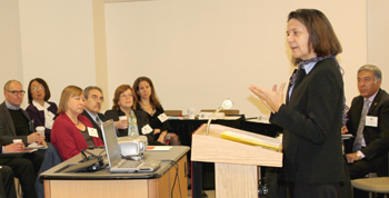 Female CEO at podium, addressing small crowd at forum event.