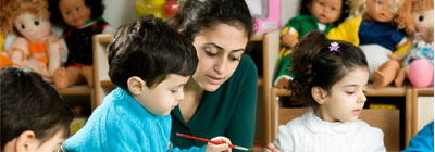 A female teacher assists young children.
