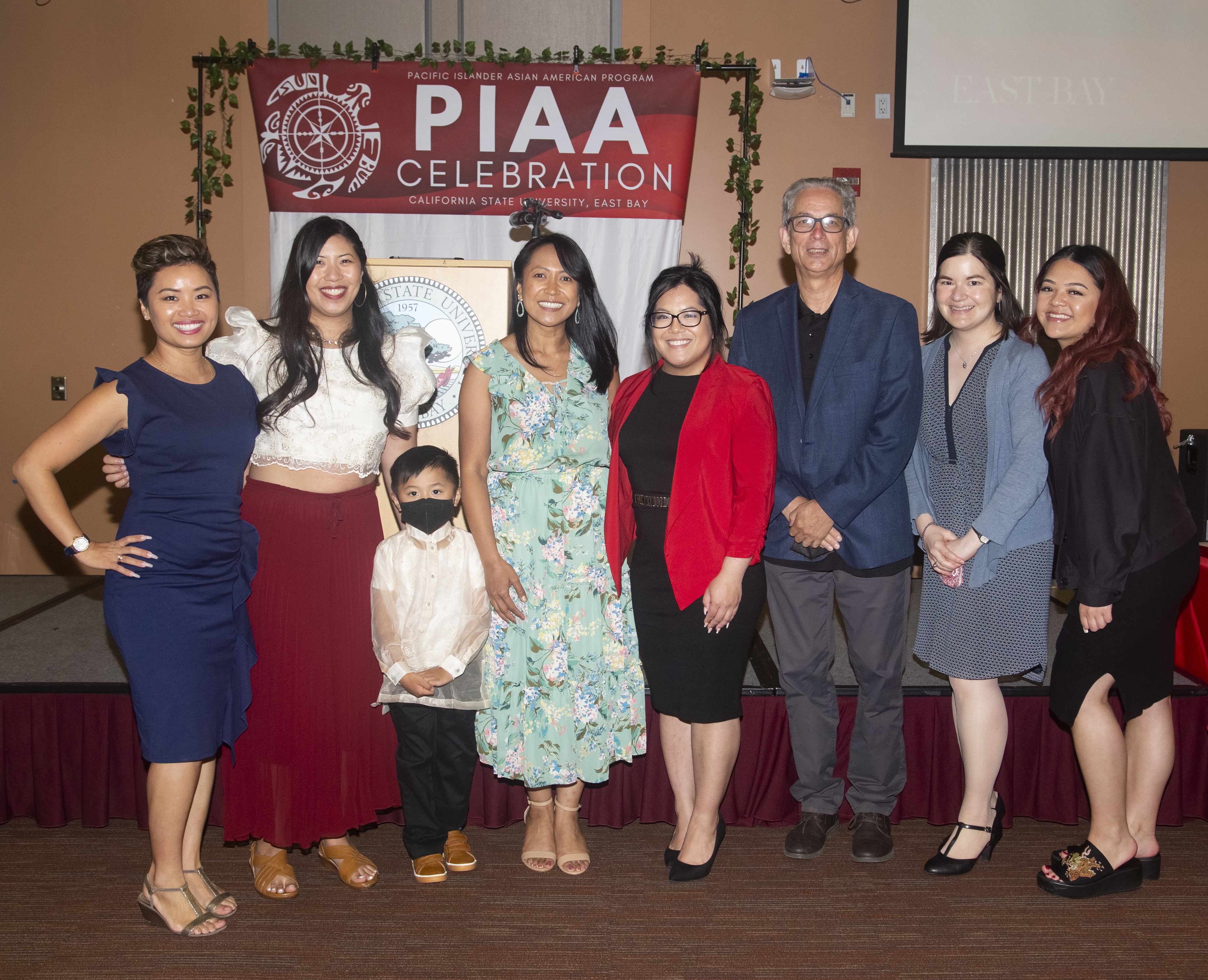 PIAA staff, faculty, and community members posing in front of a stage and "PIAA celebration" banner