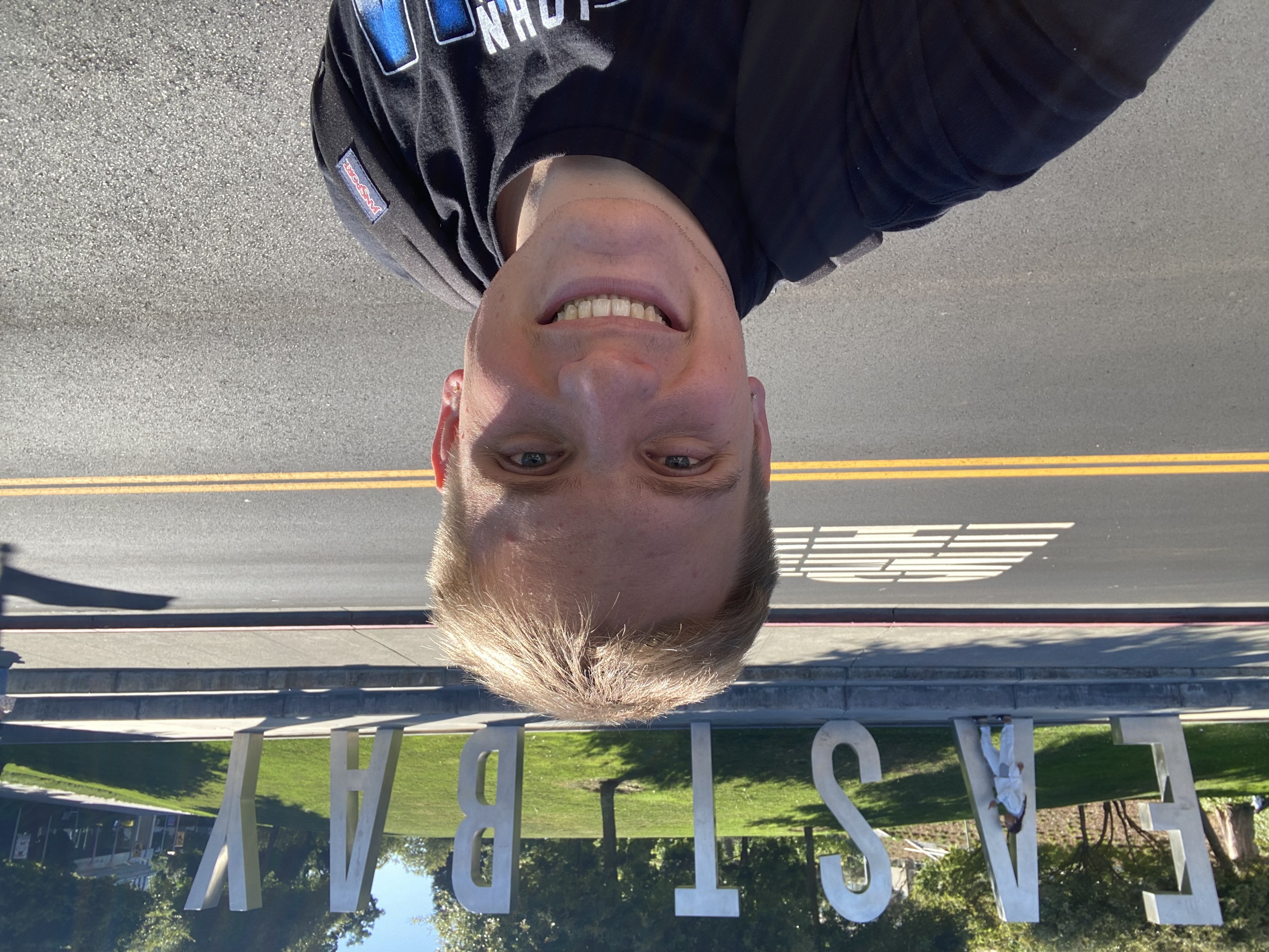 Picture of Aiden, white blonde-haired male standing in from of East Bay Sign. 