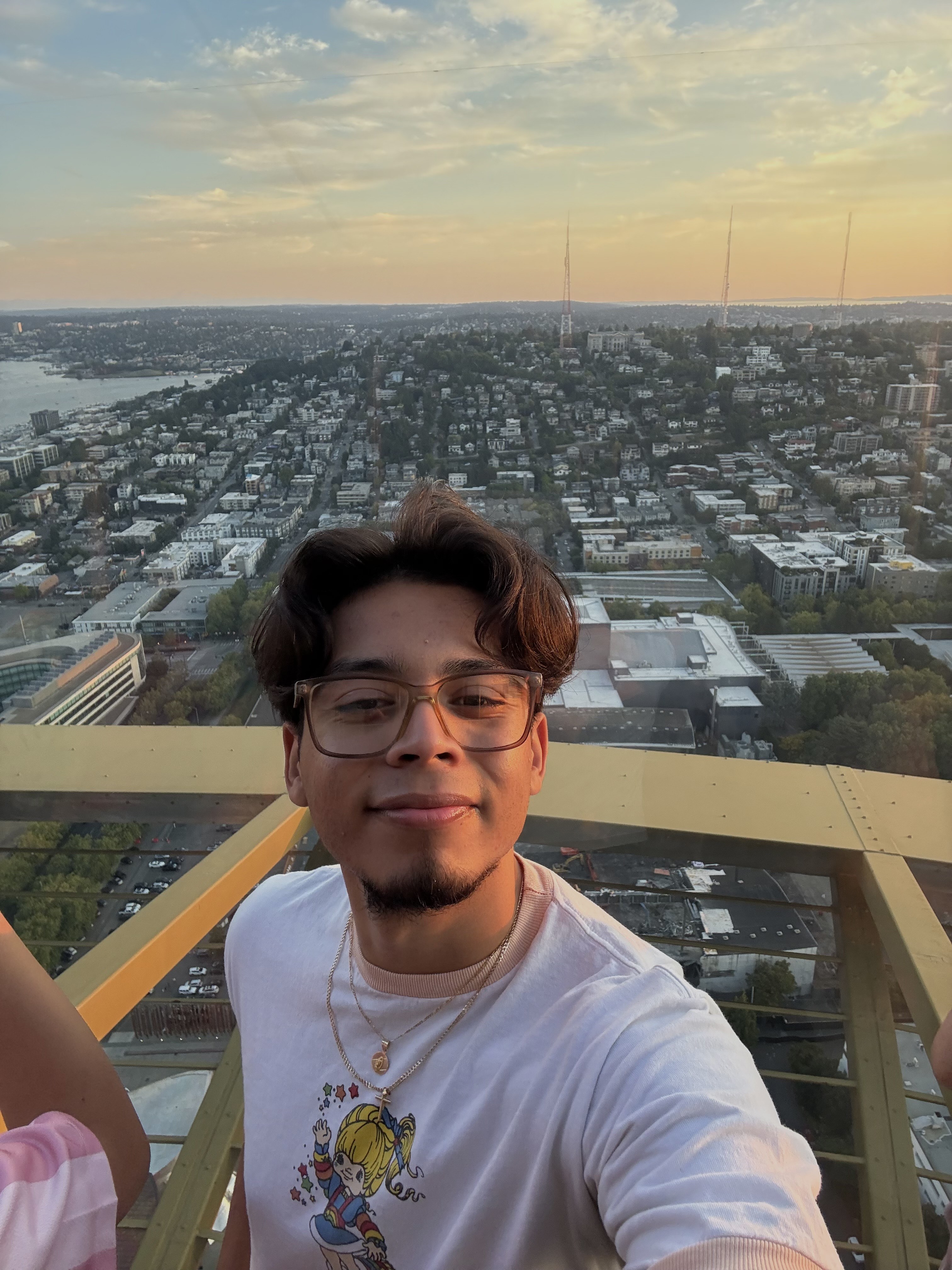 Picture of Eduardo, dark-haired Hispanic male wearing glasses, standing on roof with a sunset behind him.