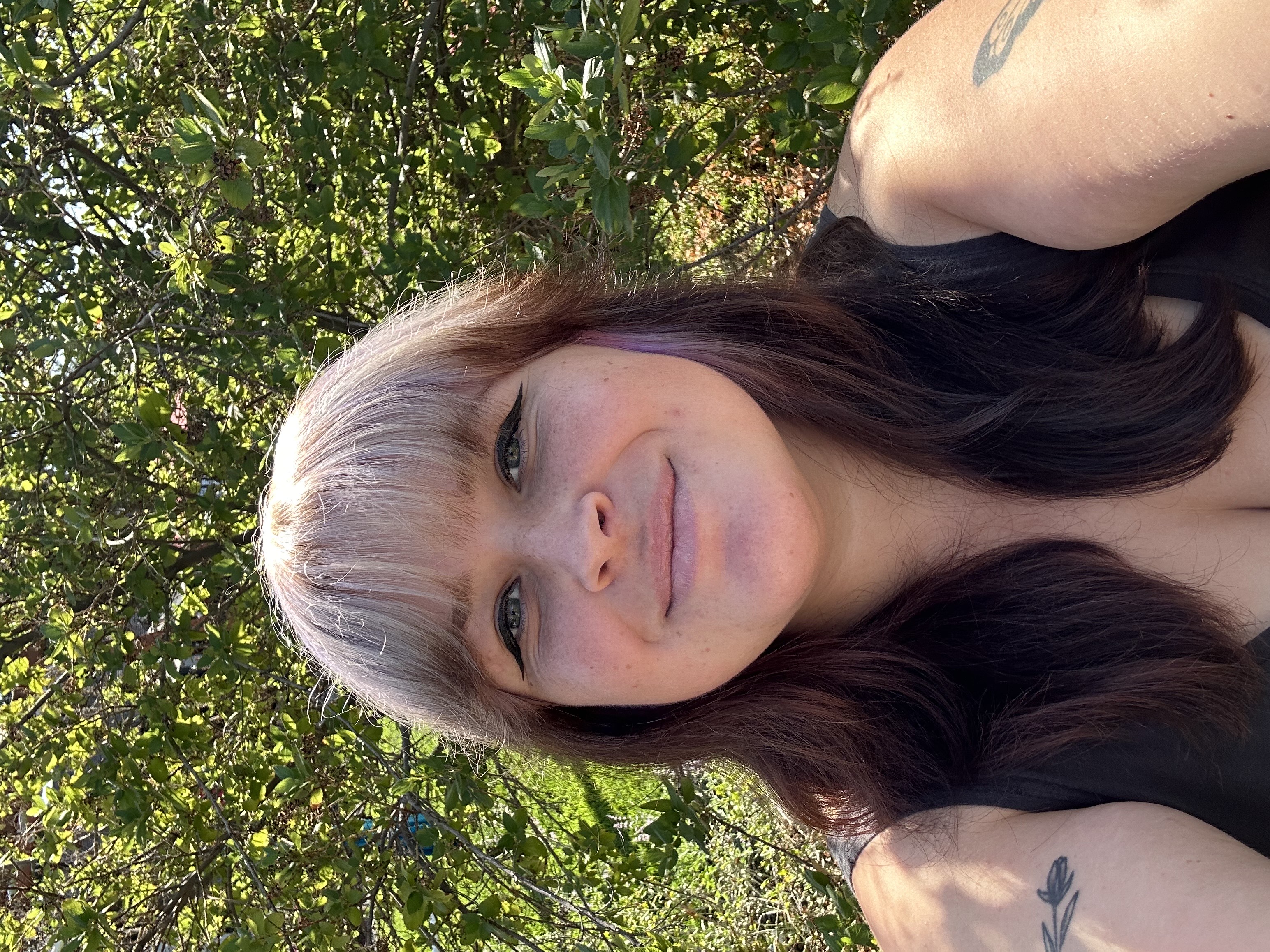 Picture of Taylor, white female with purple and black hair standing in front of tree. 