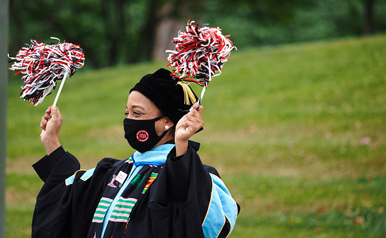 Staff member in graduation robe waves pom pom at commencement