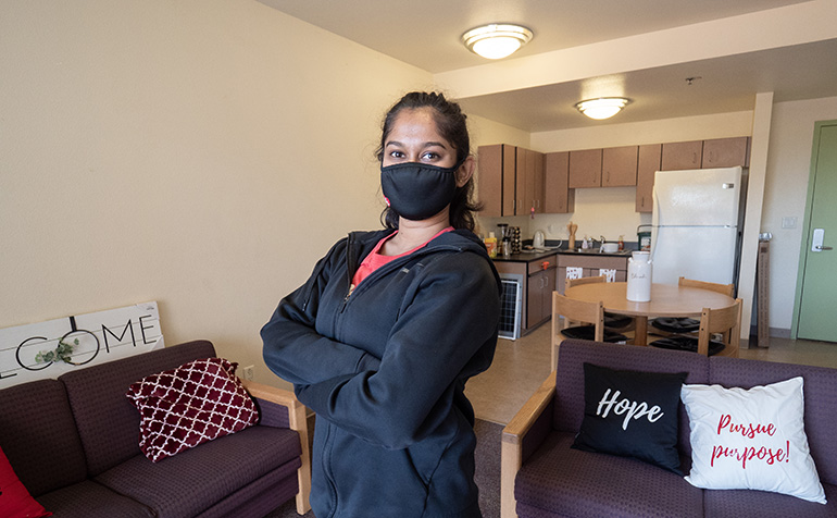 Student in mask stands in dorm room