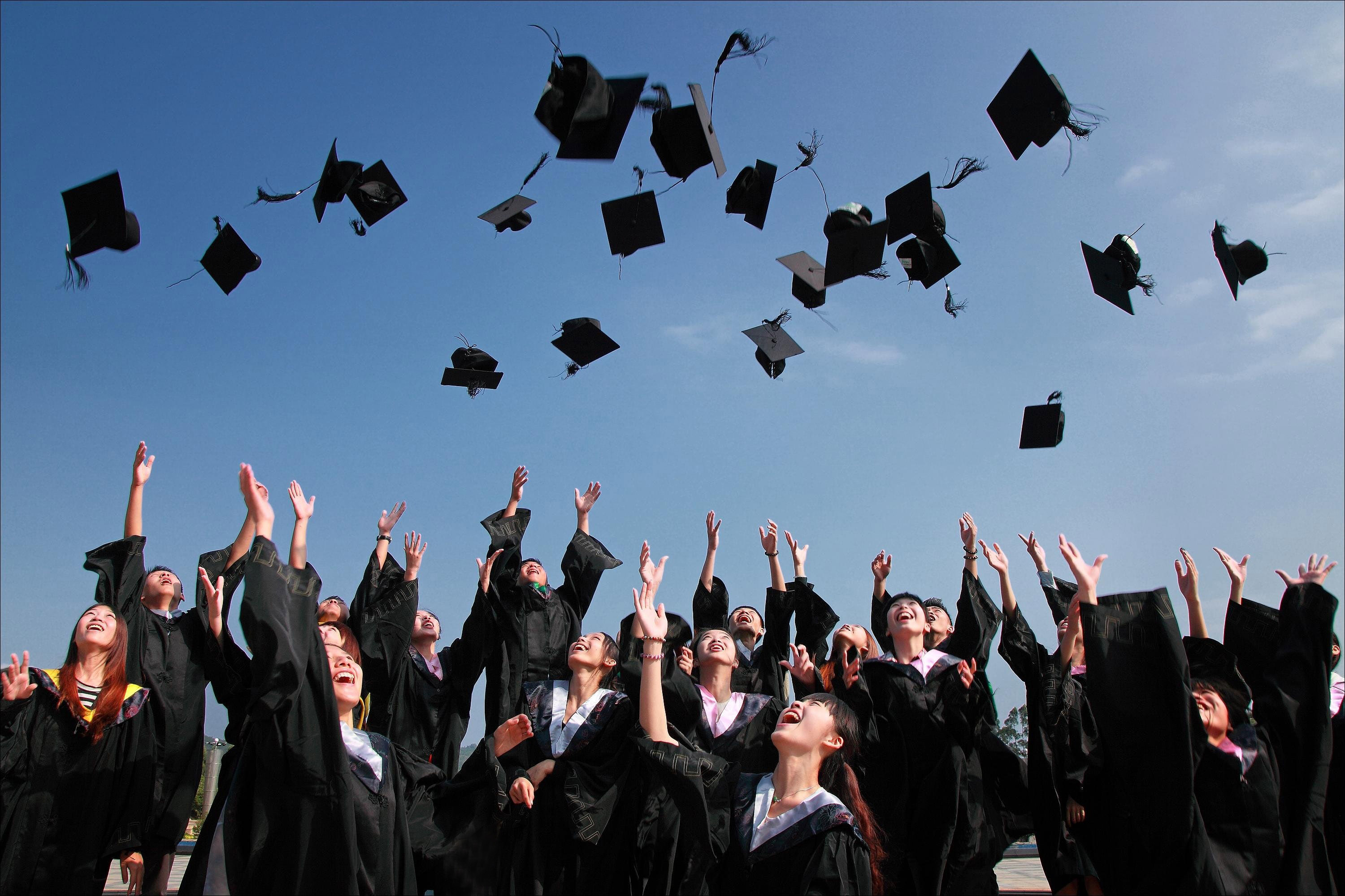 Happy college graduates throw hats in the air at graduation